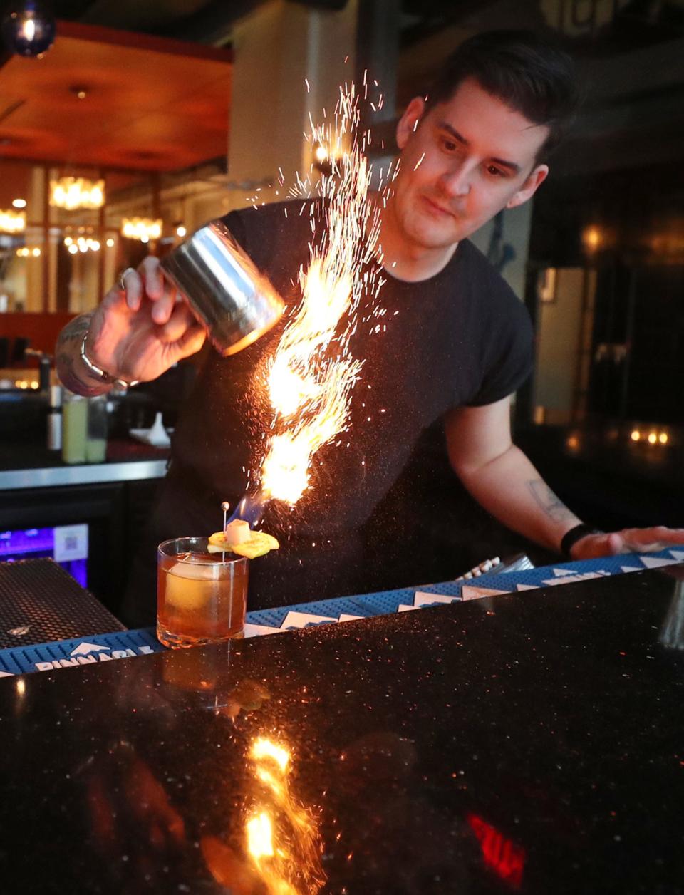 Ryan Austin, partner and mixologist at the new restaurant and bar The Circle of 5ths, makes a seasonal cocktail An Apple a Day at the restaurant located above Blue Jazz+ in Akron. The drink flames up when cinnamon is shaken over a flaming sugar cube.
