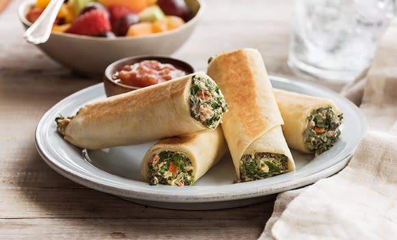 Four spinach roll-ups with dipping sauce in white porcelain bowl.