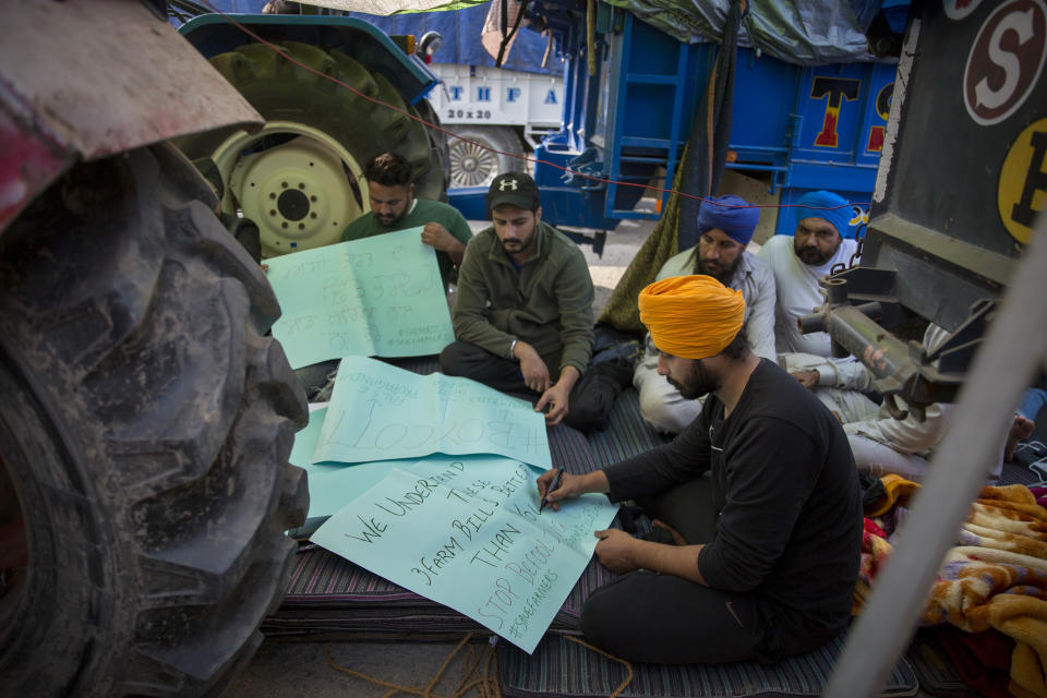 Young farmers make placards as they block a major highway during a protest against new farming laws they say will result in exploitation by corporations, eventually rendering them landless, at the Delhi-Haryana state border, India, Tuesday, Dec. 1, 2020. The busy, nonstop, arterial highways that connect most northern Indian towns to this city of 29 million people, now beat to the rhythm of never-heard-before cries of "Inquilab Zindabad" ("Long live the revolution"). Tens and thousands of farmers, with colorful distinctive turbans and long, flowing beards, have descended upon its borders where they commandeer wide swathes of roads. (AP Photo/Altaf Qadri)