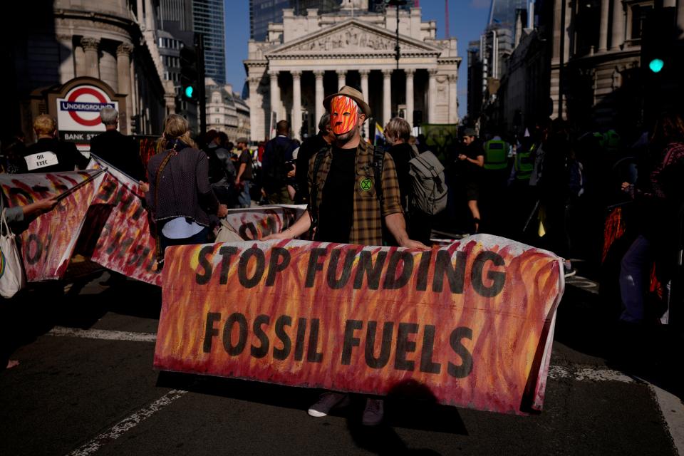 A climate change activist with Extinction Rebellion holds a banner backdropped by the Bank of England, at left, and the Royal Exchange, center, in the London financial district.