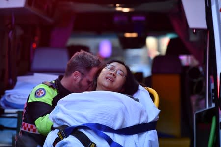 A woman is taken by ambulance, as police officers investigate a scene following reports of a stabbing in Sydney