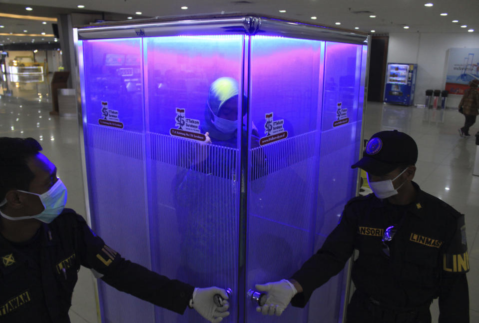 A woman stands inside a sterilization chamber set up at the arrival hall of Juanda International Airport amid new coronavirus outbreak, in Surabaya, Indonesia, Tuesday, March 24, 2020. The new coronavirus causes mild or moderate symptoms for most people, but for some, especially older adults and people with existing health problems, it can cause more severe illness or death. (AP Photo)