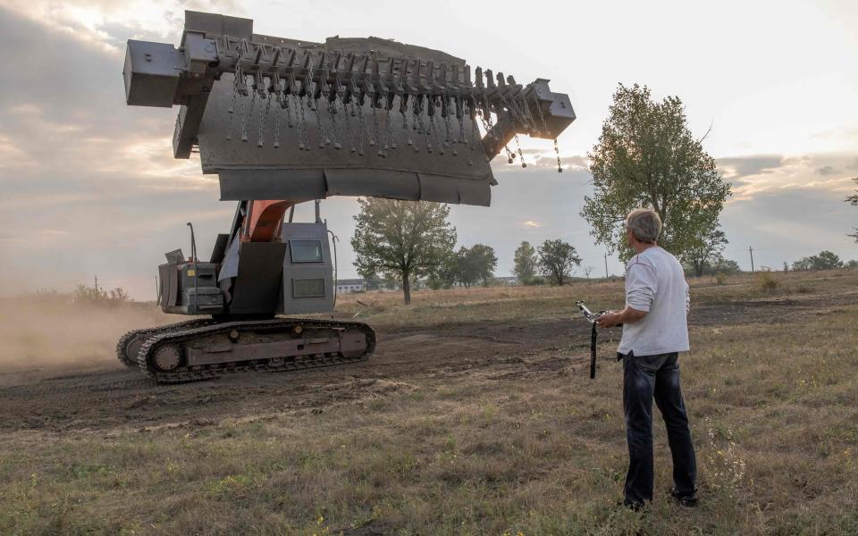 A man using a remote control demonstrates an up-armored excavator for demining purposes, in Kryvyi Rig