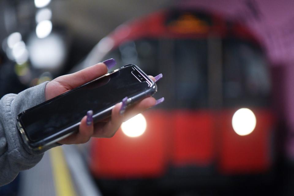 A woman uses a phone on the underground in London. (PA)