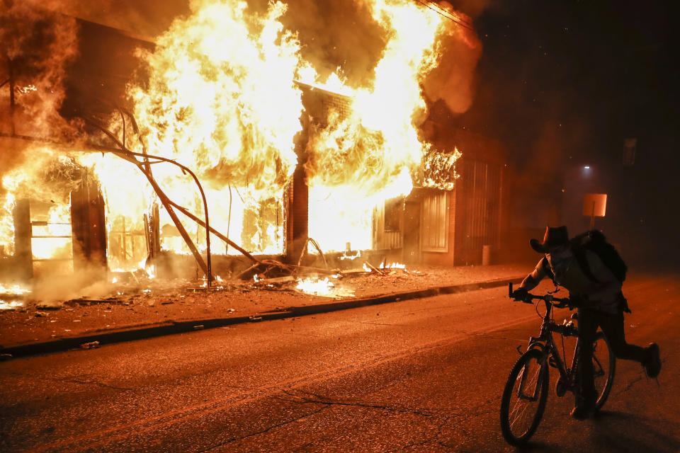 A protester rides his bike past a burning building that housed a check cashing business, Friday, May 29, 2020, in St. Paul, Minn. Protests continued following the death of George Floyd, who died after being restrained by Minneapolis police officers on Memorial Day. (AP Photo/John Minchillo)