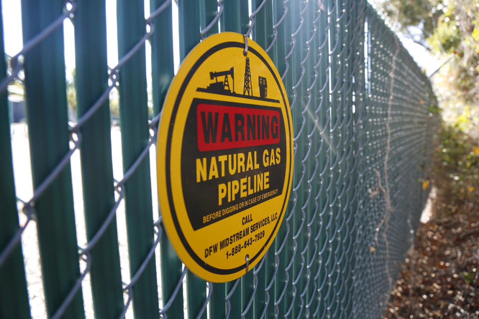 A warning sign marks a natural gas pipeline outside a compressor station on Monday, Oct. 25, 2021, in Dalworthington Gardens, Texas, a small municipality that's tucked within the city of Arlington. Compressor stations like this one change the pressure of the natural gas to help move it through the lines. Increasingly, natural gas ends up at facilities on the Gulf Coast where it is converted into liquid natural gas, or LNG, so it can be shipped to Europe, Asia and other parts of the world. Natural gas is used to heat homes and for cooking, among other things. (AP Photo/Martha Irvine)