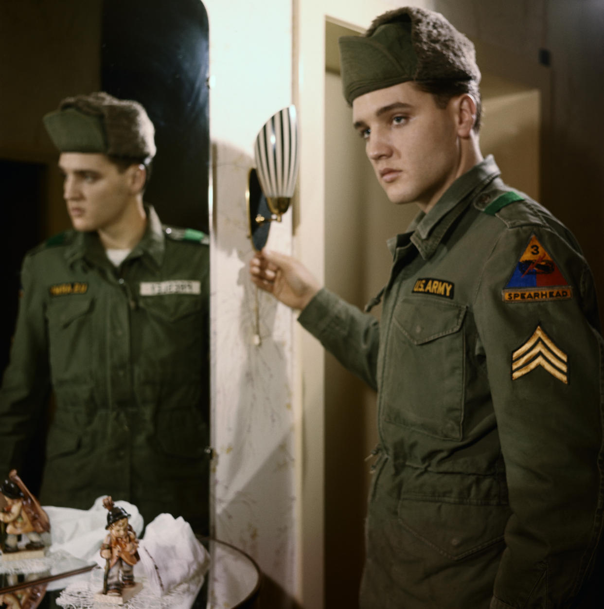 (Original Caption) Friedberg, Germany: Wearing a serious expression, singer Elvis Presley points to his three stripes after he was promoted to acting Sergeant here January 20th. He was promoted from the rank of Specialist Fourth Class and the advancement carries no increase in pay.