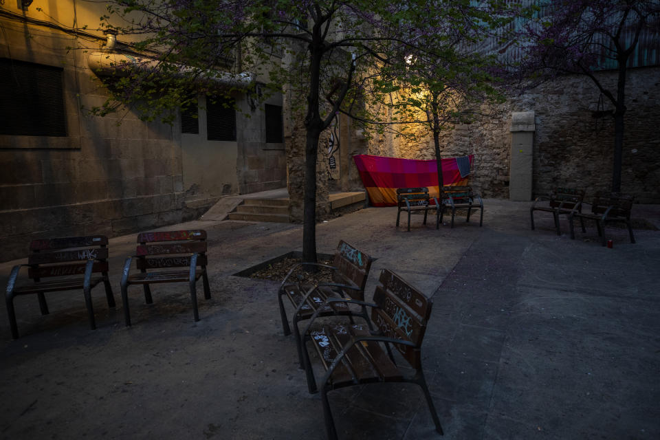 In this Saturday, March 21, 2020 photo, a blanket is used as a shelter in the corner of a square in downtown Barcelona, Spain. With Spain one of the world's worst-hit countries by the new coronavirus, and the government ordering a national lockdown, the country's streets are largely deserted. (AP Photo/Emilio Morenatti)