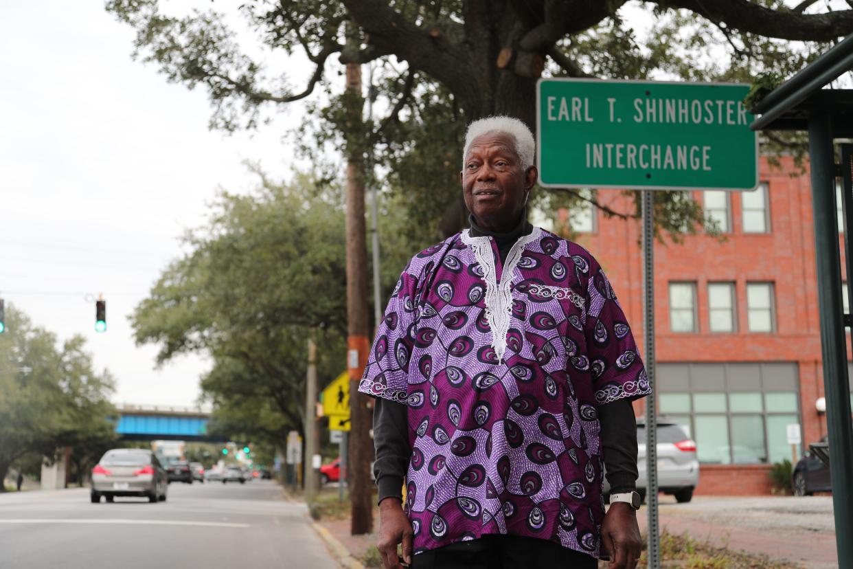 Richard Shinhoster, owner of Diaspora Marketplace, stands on Martin Luther King, Jr Boulevard near his business and the sign showing that the I-16 interchange is named in honor of his brother Earl.