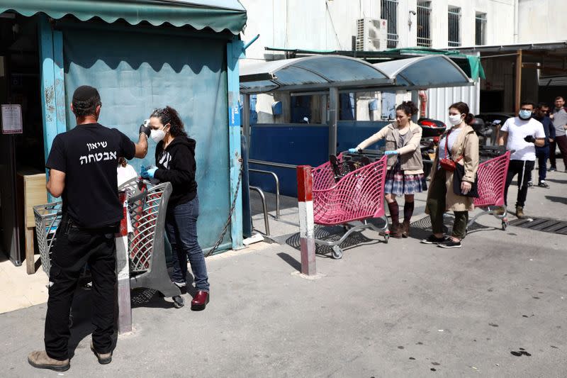 A guard checks a woman's temperature before she enters a supermarket to shop ahead of the Jewish holiday of Passover, amid the coronavirus disease (COVID-19) outbreak in Jerusalem