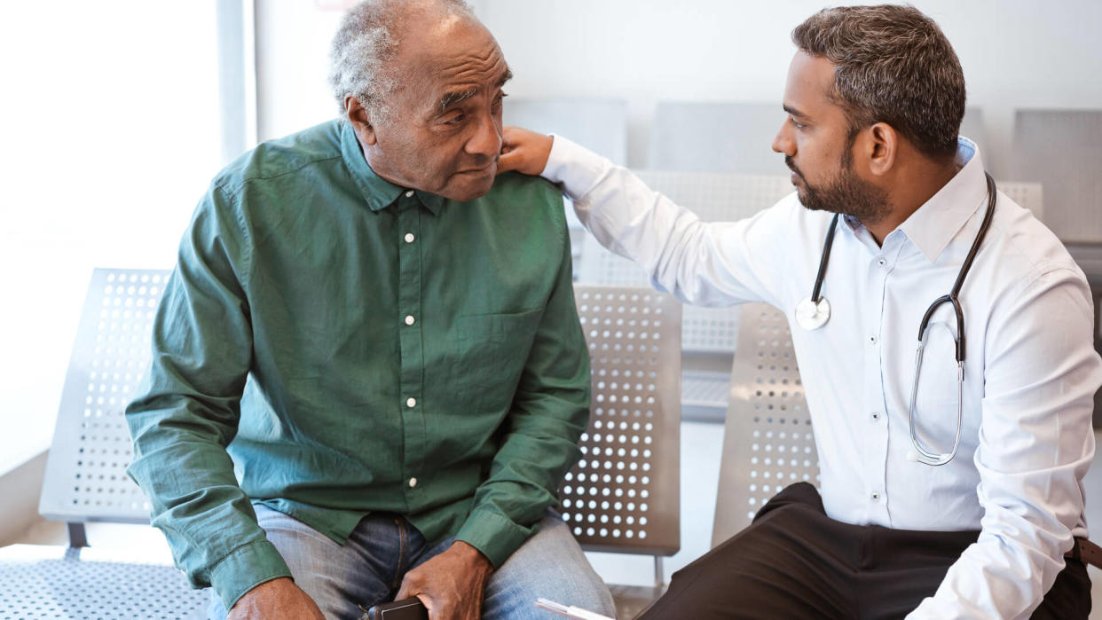 Healthcare worker giving bad news with hand on shoulder of male patient.