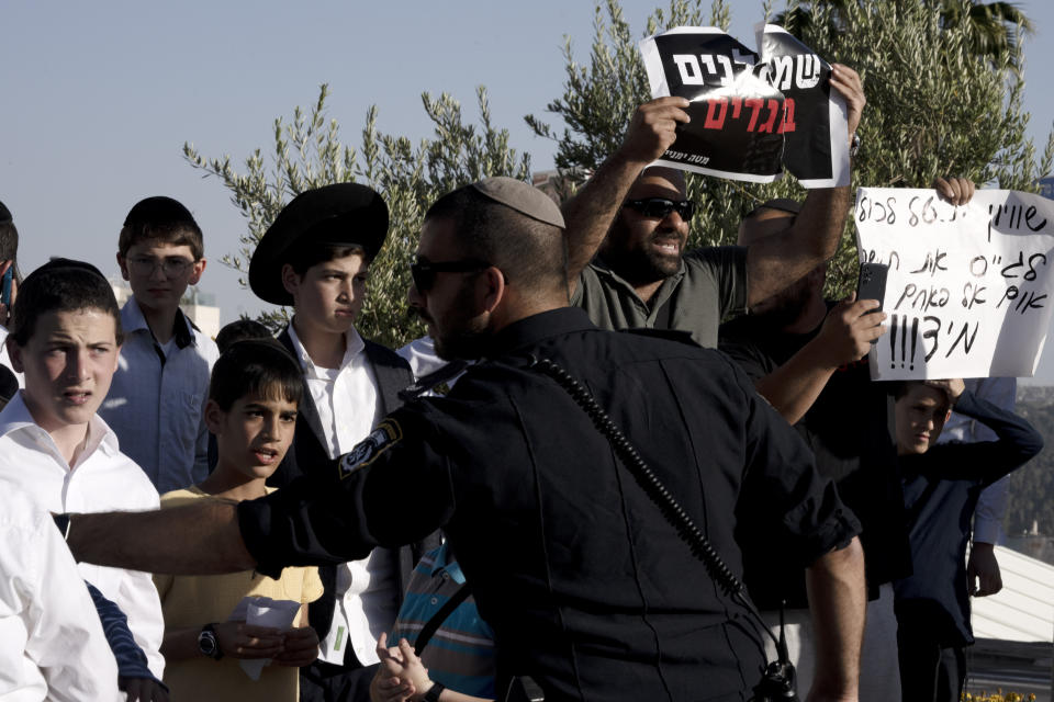 FILE - Untra-Orthodox youth and right-wing activists state a counter-protest as mothers wearing Israel Defense Forces unit berets during a protest against a proposed military draft bill exempting ultra-Orthodox Jews from military service outside an ultra-Orthodox seminary, in Jerusalem, Thursday, May 4, 2023. With ultra-Orthodox parties now wielding unprecedented power and playing a key role in a contentious plan to overhaul the legal system, they are aggravating concerns among secular Israelis that the character and future of their country is under threat. (AP Photo/Maya Alleruzzo, File)