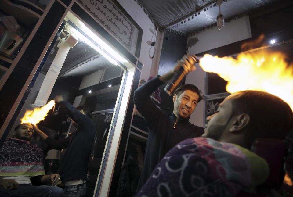 In this Wednesday, March 15, 2017 photo, Palestinian hair dresser Ramadan Adwan uses fire to straighten the hair of a costumer in his barber shop in Rafah refugee camp in the Gaza Strip. After cutting and combing, the barber applies what he calls "special" lotion and powder client's heads to protect their skin before using an aerosol can to burn hair off. (AP Photo/ Khalil Hamra)