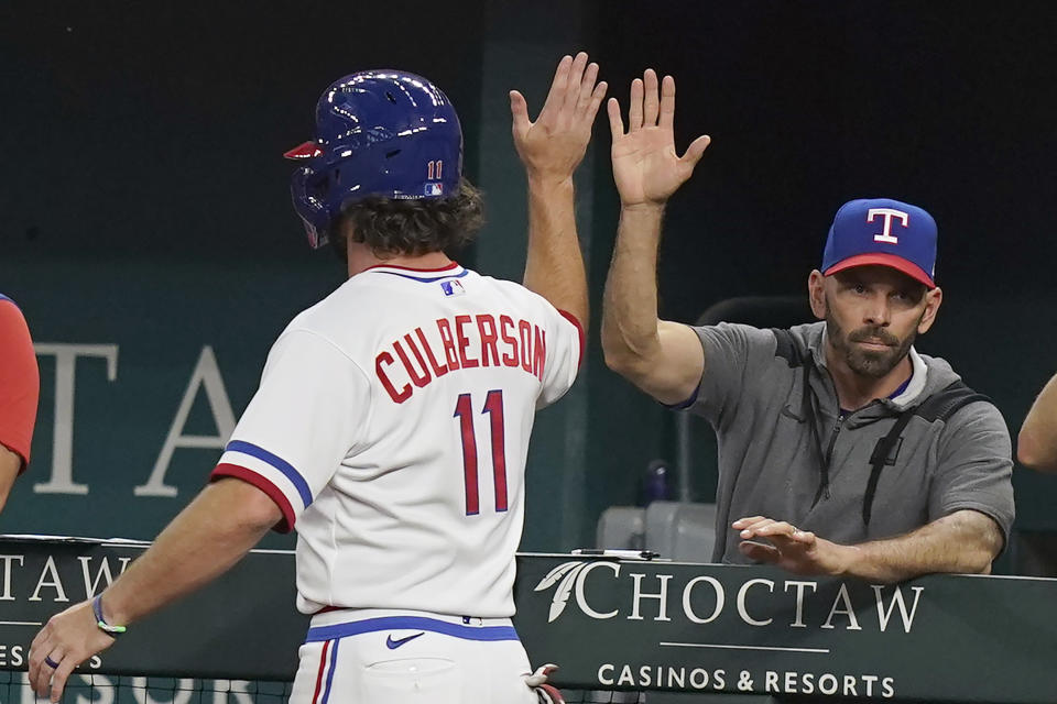 Texas Rangers' Charlie Culberson (11) gets a high five from manager Chris Woodward after scored on a sacrifice bunt by teammate Bubba Thompson during the fourth inning of a baseball game against the Seattle Mariners in Arlington, Texas, Saturday, Aug. 13, 2022. (AP Photo/LM Otero)