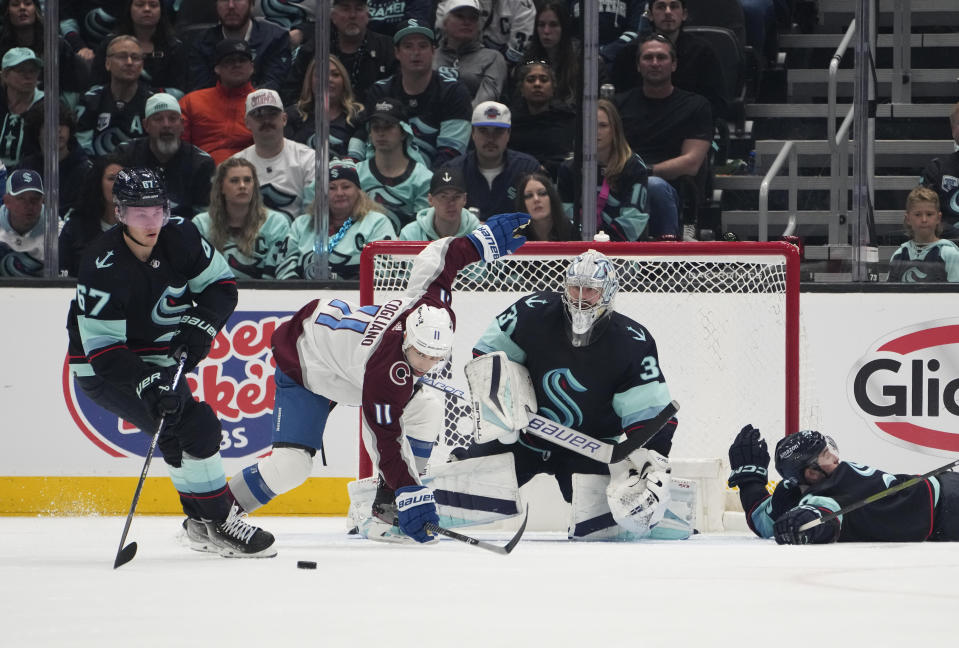 Seattle Kraken center Morgan Geekie (67) clears the puck as Colorado Avalanche center Andrew Cogliano (11) trips near the goal and Kraken goaltender Philipp Grubauer (31) watches during the third period of Game 6 of an NHL hockey Stanley Cup first-round playoff series Friday, April 28, 2023, in Seattle. The Avalanche won 4-1. (AP Photo/Lindsey Wasson)