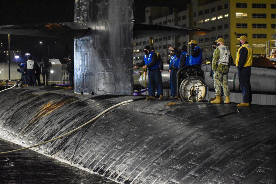 Sailors on the USS Oklahoma City work with dock workers to pull in and stabilize the 361 foot vessel.