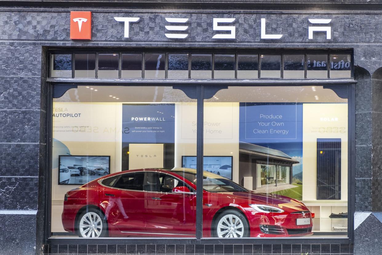 Tesla showroom located on the corner of the Hobbemastraat and PC Hooftstraat in Amsterdam. A Red Tesla Model S full-sized electric five-door hatchback is on display inside. People in the foreground are looking at the car.