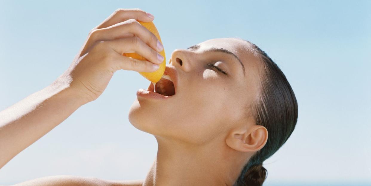 young woman squeezing juice from orange into mouth, close up