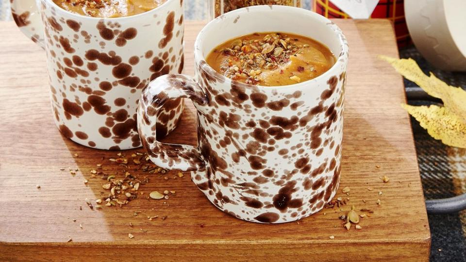 savory pumpkin soup in two brown and white mugs with spice shake on top