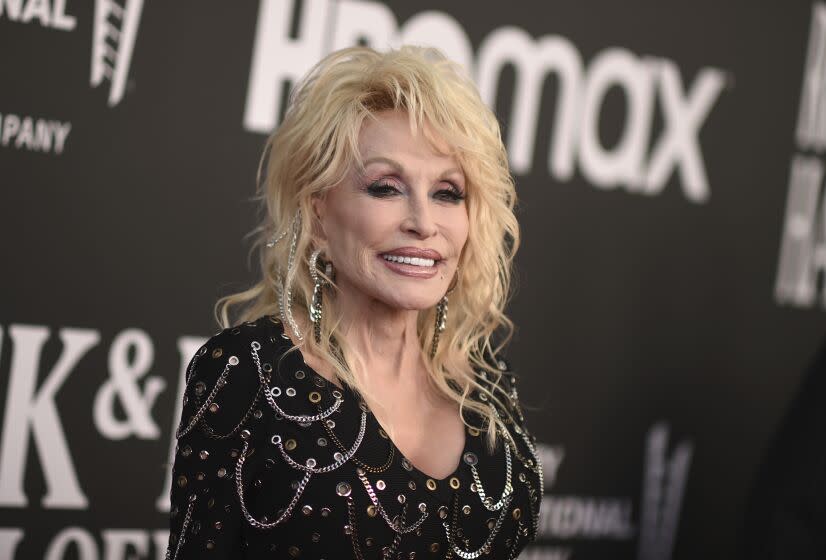 A woman with wavy blond hair smiling in a black, bedazzled dress