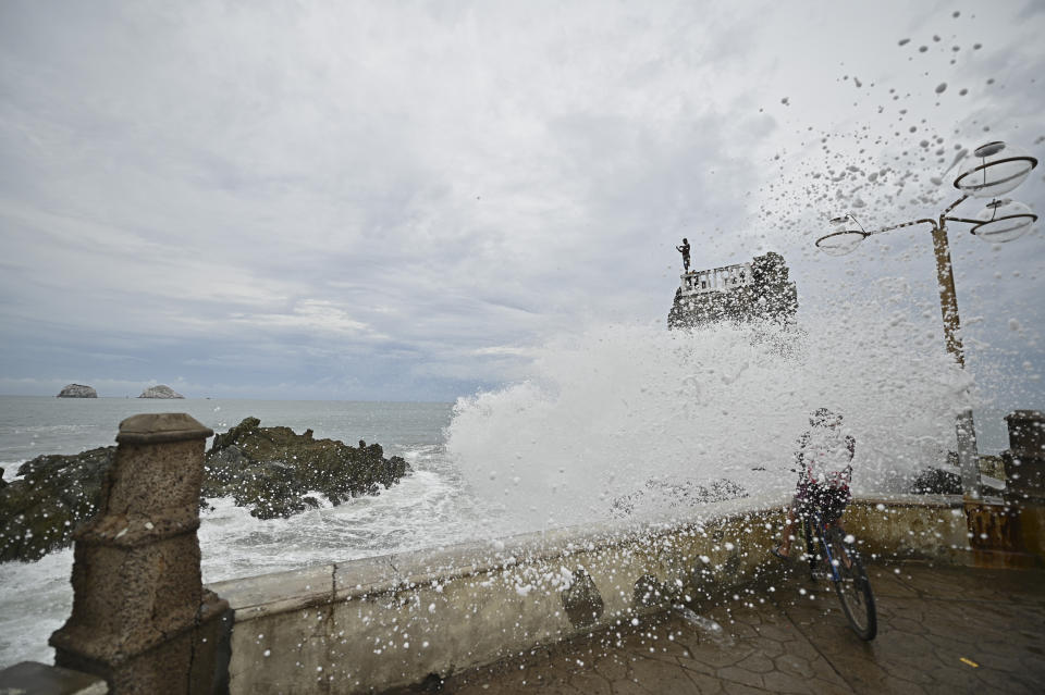 A cyclist is splashed by a crashing wave prior the landfall of tropical storm Pamela, on the boardwalk in Mazatlan, Mexico, Tuesday, Oct. 12, 2021. Hurricane Pamela weakened to a tropical storm Tuesday afternoon as it meandered off Mexico's Pacific coast. Forecasters said it was expected to regain strength overnight and be a hurricane when making landfall somewhere near the port of Mazatlan Wednesday. (AP Photo/Roberto Echeagaray)