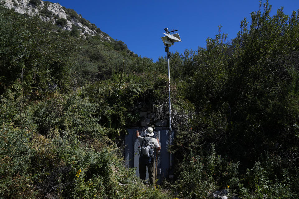 Gary Earney, retired forester with the U.S. Forest Service, touches the door of an area where BlueTriton collects spring water in the San Bernardino National Forest on Monday, Sept. 18, 2023, in San Bernardino, Calif. Earney handled water permits for springs in that area from 1978-2007. The State Water Resources Control Board is expected to vote Tuesday on whether to issue a cease-and-desist order against BlueTriton, the company that produces the widely-known Arrowhead brand of bottled water. The order would prevent BlueTriton from drawing water from certain points in the San Bernardino National Forest. (AP Photo/Ashley Landis)