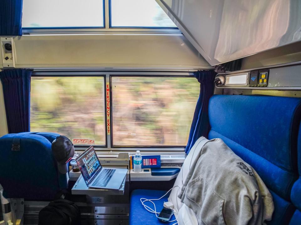 Inside an Amtrak bedroom with blue seats and a big window showing nature outside
