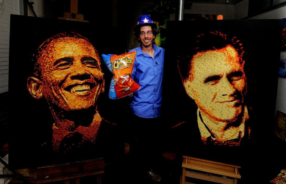 IMAGE DISTRIBUTED FOR CHEETOS - Artist Jason Baalman poses in front of portraits of President Barack Obama and former Gov. Mitt Romney made entirely of more than 2,000 individual Cheetos snacks Tuesday, Oct. 2, 2012, in Baalman’s Colorado Springs, Colo., studio.  Today, the Cheetos brand unveiled a new electoral polling model with the unveiling of 3 feet by 4 feet one-of-a-kind Cheetos portraits of the Democratic and Republican presidential nominees – President Barack Obama and former Gov. Mitt Romney. Debuting on Facebook today at 11 a.m. CT, fans are encouraged to vote for their candidate’s portrait – made entirely of more than 2,000 individual Cheetos cheese snacks – for a chance to win the actual portrait. (Photo by Jack Dempsey/Invision for Cheetos/AP Images)