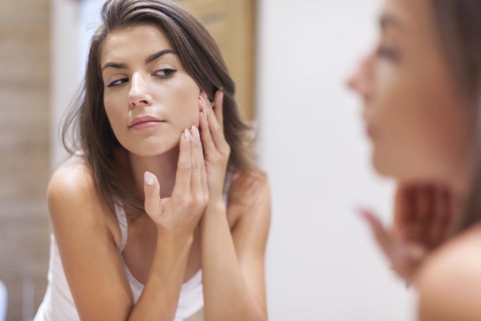 A woman examines her skin in the mirror