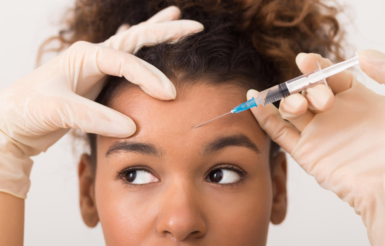 Someone wearing medical gloves holds a needle to a woman's forehead.