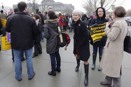 Former U.S. Health and Human Services Secretary Kathleen Sebelius (C) walks between demonstrators as she arrives at the Supreme Court building in Washington March 4, 2015. REUTERS/Jonathan Ernst