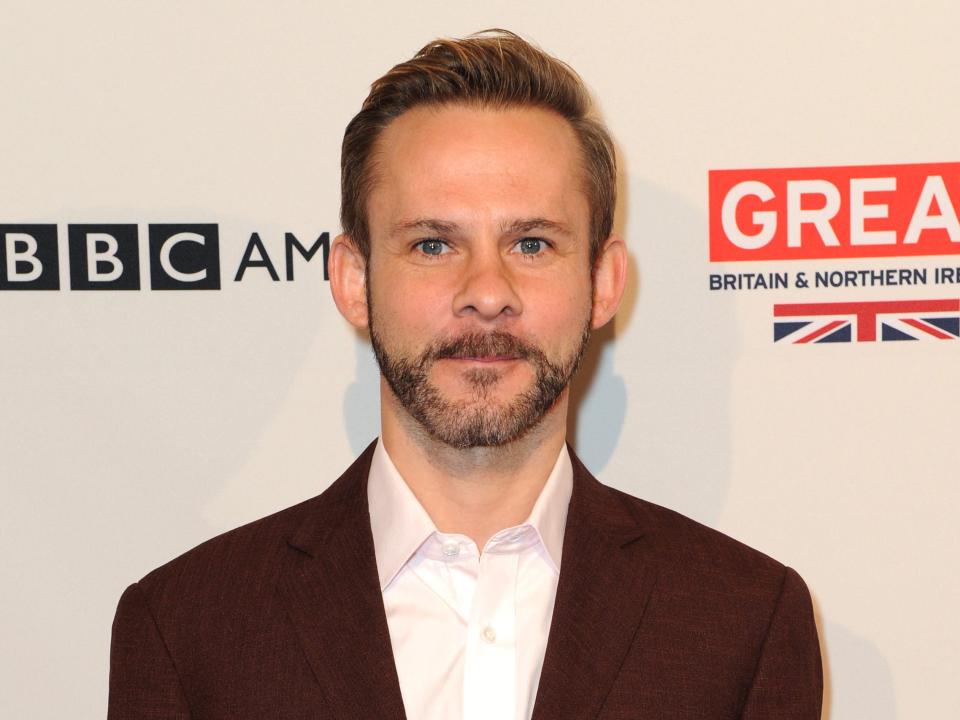 Dominic Monaghan wearing a reddish brown suit in fruit of a white background