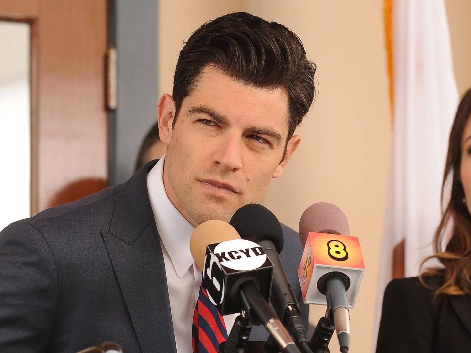 Max Greenfield as Schmidt behind a lectern with microphones