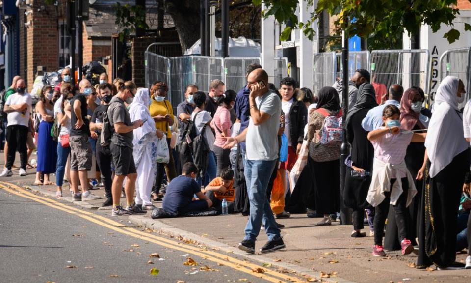 A queue of people in the street, close together, wearing masks