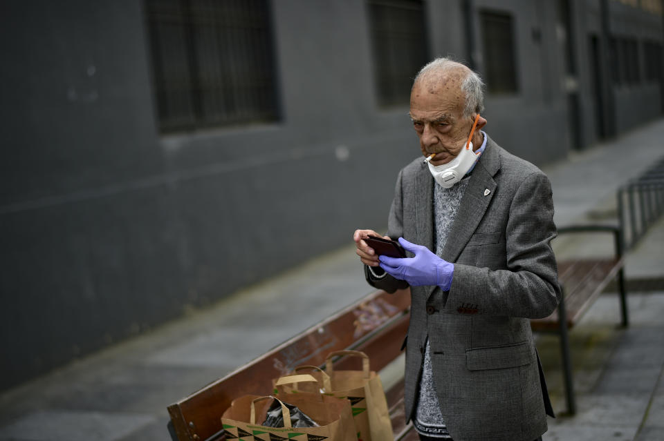 An elderly man coves partially his face with a mask protection to prevent the spread of the coronavirus, smokes a cigarette, in Pamplona, northern Spain, Saturday, May 2, 2020. Spain relaxed its lockdown measures Saturday, allowing people of all ages to leave their homes for short walks or exercise for the first time since March 14.(AP Photo/Alvaro Barrientos)