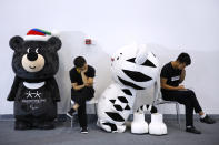 Workers browse their phones next to the mascots for the 2018 Pyeongchang Winter Olympics and Paralympic Games near the South Korean booth during the World Winter Sports Expo in Beijing, Sept. 7, 2017. (AP Photo/Andy Wong)