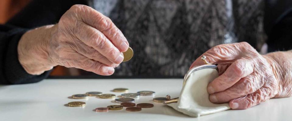 Elderly 95 years old woman sitting miserably at the table at home and counting remaining coins from the pension in her wallet after paying the bills.