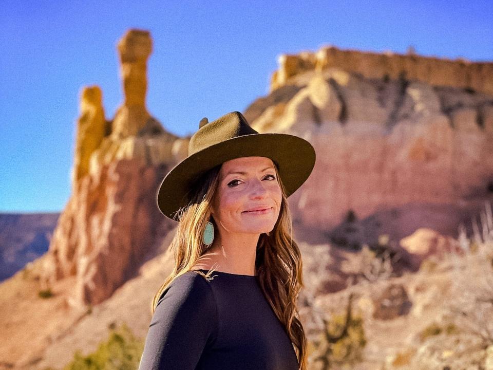 Emily, wearing jeans, a long-sleeved black shirt, and a hat, stands in front of rock formations at Ghost Ranch.