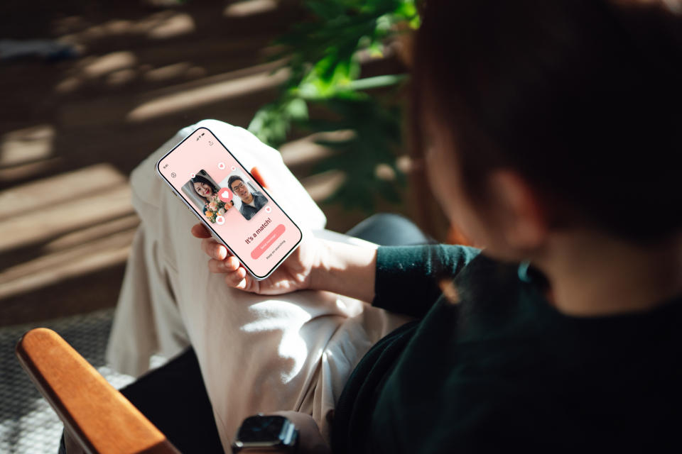 Over the shoulder view of young woman using dating app to match a date with smartphone. Online dating. Love and romance concept.