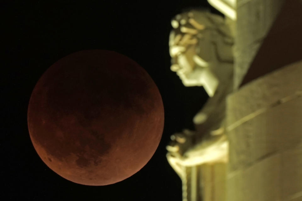 A lunar eclipse covers the moon as it rises beyond a statue atop the Liberty Memorial tower at the National World War I Museum on Monday, May 16, 2022, in Kansas City, Mo. (AP Photo/Charlie Riedel)