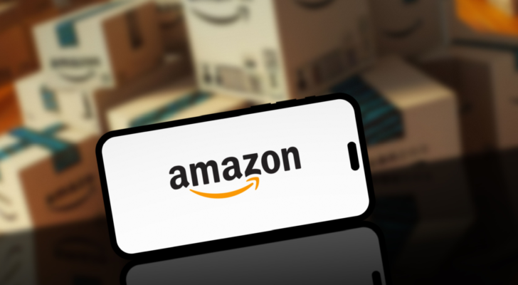 Amazon logo on smartphone screen with blurred Amazon delivery or shipping boxes in the background. AMZN stock