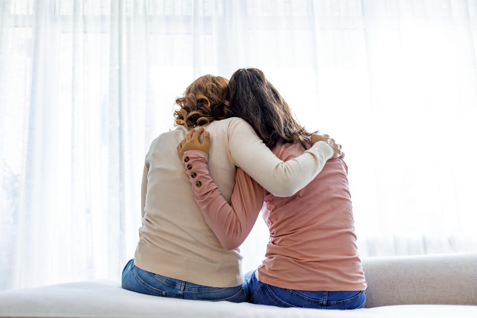 Rear back viewof a mother and daughter embrace sitting on bed at home, older sister consoling younger teen, girl suffers from unrequited love share secrets trustworthy person relative people concept