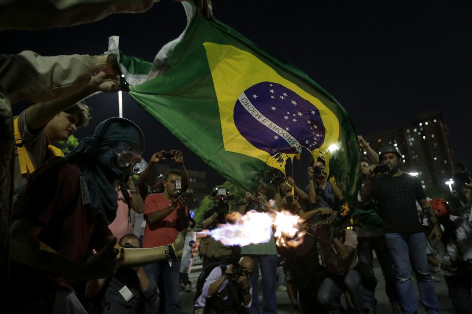 Demonstrators burn a Brazilian flag during a protest against the 2014 World Cup in Rio de Janeiro May 15, 2014. Brazilians opposed to the World Cup and the public funds spent on the construction of stadiums called for a day of protests around the country. REUTERS/Ricardo Moraes (BRAZIL - Tags: SOCIETY SPORT SOCCER WORLD CUP CIVIL UNREST)