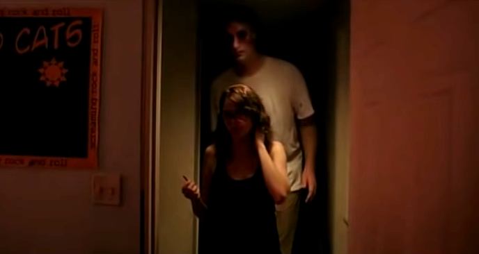 A very tall man following a woman down a dark hallway