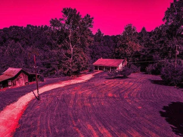 a small house surrounded bya. lawn and a long dirt driveway and trees, the entire image lit in magenta