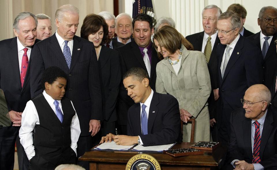 FILE - In this March 23, 2010, file photo, Marcelas Owens of Seattle, left, Rep. John Dingell, D-Mich., right, and others, watch as President Barack Obama signs the health care bill in the East Room of the White House in Washington. A closely watched survey says the nation’s uninsured rate dropped modestly this month as the major coverage expansion under Obama’s health care law got underway. The Gallup-Healthways Well-Being Index found that the uninsured rate for U.S. adults dropped by 1.2 percentage points in January, to 16.1 percent. The rate declined across major groups. (AP Photo/J. Scott Applewhite, File)