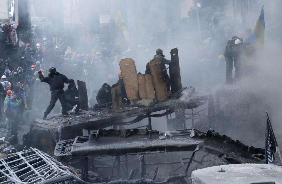 Protesters protect themselves from water guns, as one of them throws a stone, during a clash with riot police in central Kiev, Ukraine, Saturday Jan. 25, 2014. Ukraine's Interior Ministry has accused protesters in Kiev of capturing two of its officers as violent clashes have resumed in the capital and anti-government riots spread across Ukraine. (AP Photo/Efrem Lukatsky)