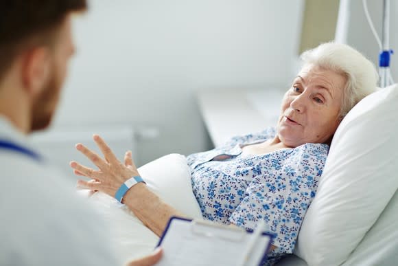 Senior woman lying in bed, talking to a doctor