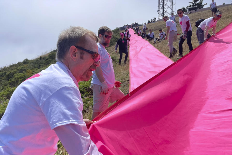 Patrick Carney, left, Co-Founder of Friends of the Pink Triangle, works with volunteers laying out pink tarps to form the shape of a pink triangle on Twin Peaks in San Francisco, Friday, June 16, 2023. Hundreds of volunteers installed the giant pink triangle made out of cloth and canvas and with pink lights around its edges last week as part of the city's Pride celebrations. It's an annual tradition that started in 1995 but this year's triangle is nearly an acre in size and can be seen up to 20 miles (32 kms.) away. (AP Photo/Haven Daley)