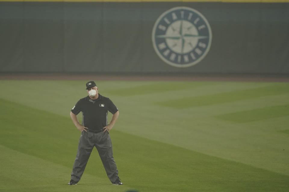 Second base umpire Bill Miller wears a mask as he stands on the field in air hazy from wildfire smoke during the first baseball game of a doubleheader between the Seattle Mariners and the Oakland Athletics, Monday, Sept. 14, 2020, in Seattle. (AP Photo/Ted S. Warren)